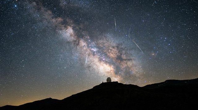 Un cielo nocturno estrellado sobre las siluetas de las montañas de Sierra Nevada en España con varios trazos brillantes de las Perseidas cruzando el firmamento