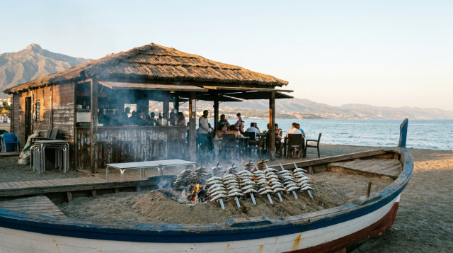 Un chiringuito tradicional de madera en una playa de la Costa del Sol con espetos de sardinas asándose en una barca de arena