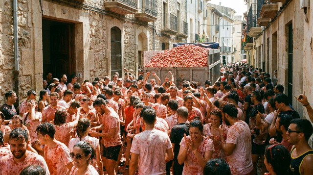 Multitud de personas cubiertas de tomate rojo celebrando la Tomatina en las calles de Buñol con un camión al fondo