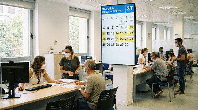 oficina de la Agencia Tributaria en España con contribuyentes gestionando trámites fiscales y calendario oficial en pantalla