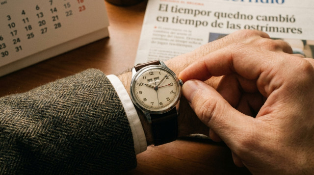 primer plano de un reloj de pulsera mecánico marcando las tres de la madrugada mientras una mano ajusta las agujas para el cambio de hora de octubre en España