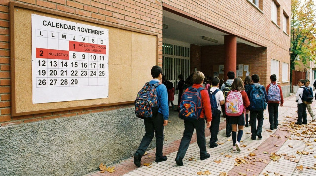 Alumnos saliendo de un colegio con mochilas frente al panel de días no lectivos de noviembre y el calendario escolar