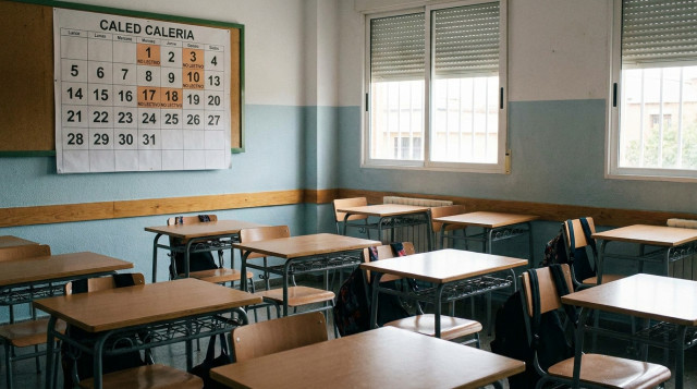 Aulas vacías de un colegio con mochilas y un calendario escolar colgado en la pared que señala las fechas no lectivas del trimestre
