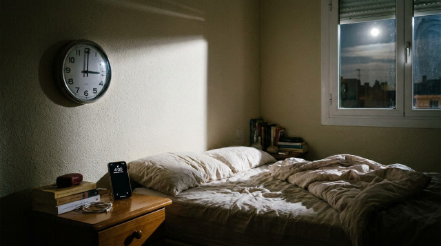 reloj analógico de pared marcando las tres de la madrugada junto a un móvil con la hora actualizada, ilustrando el cambio de hora en España