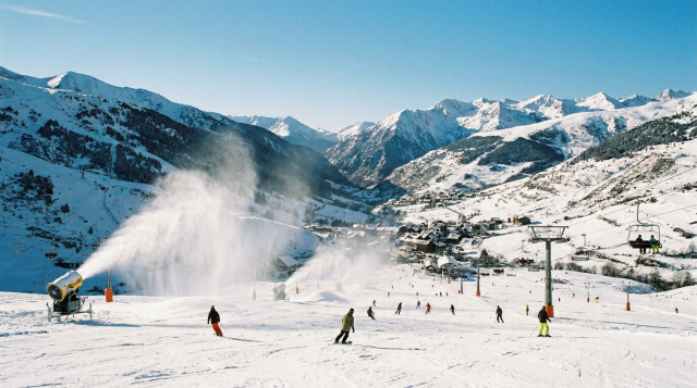 Vista panorámica de pistas de esquí en los Pirineos con esquiadores y cañones de nieve en funcionamiento