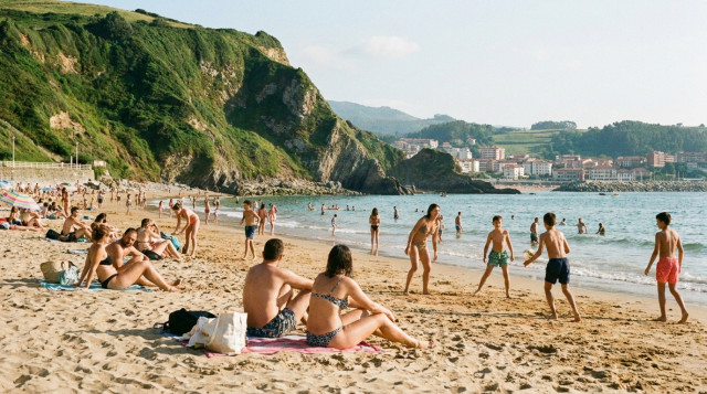 Personas disfrutando de un día festivo de julio en una playa del norte de España, con un ambiente veraniego y relajado