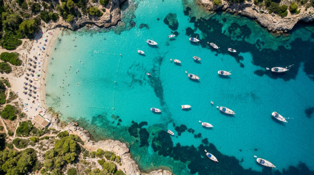 Vista a3rea de una cala de aguas turquesas en Baleares con boyas ecol3gicas delimitando la zona de ba1o y barcos fondeando correctamente fuera de la posidonia