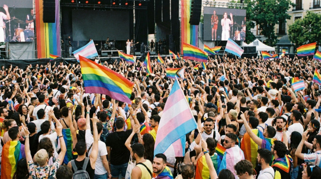 Multitud celebrando el Orgullo de Madrid en la Plaza de Pedro Zerolo con banderas de la diversidad y escenarios de conciertos al fondo