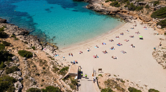 Vista aérea de una cala de aguas turquesas en España con control de aforo y bañistas distribuidos de forma ordenada en la arena