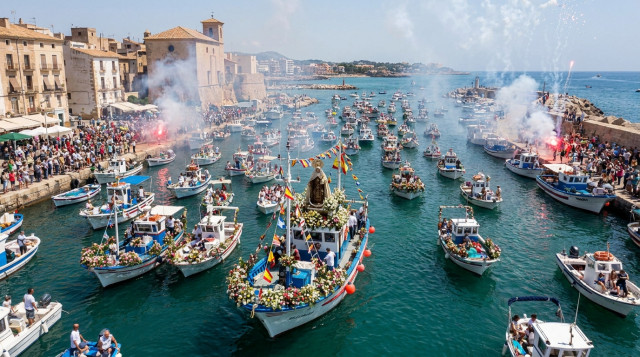 Procesión marítima de la Virgen del Carmen con barcos decorados con flores en un puerto español