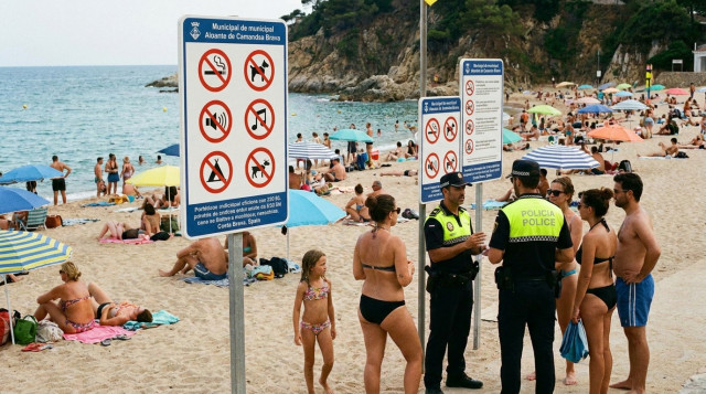 Bañistas en una playa de España con sombrillas y carteles informativos sobre las prohibiciones y multas municipales