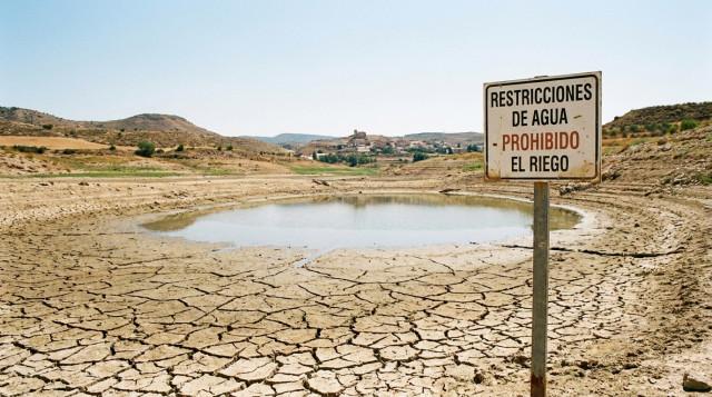 Un embalse casi seco en España con grietas en el lodo del fondo bajo un sol abrasador, ilustrando las nuevas restricciones de agua en España