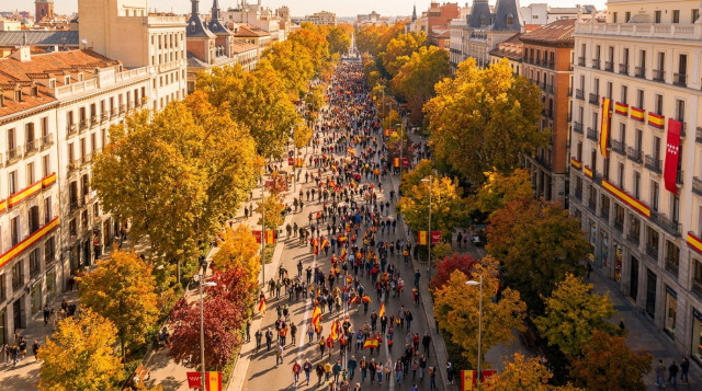 Vista aérea de una plaza en Madrid durante una jornada festiva de otoño con banderas y personas paseando