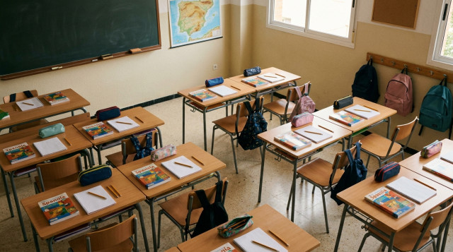 Vista cenital de un aula de colegio lista para el inicio de las clases con pupitres ordenados y material escolar sobre las mesas