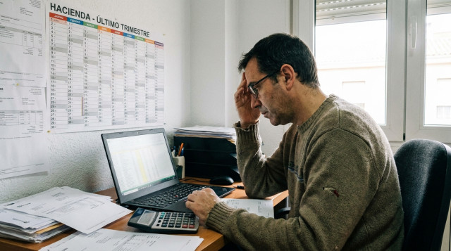 Autónomo revisando facturas y el calendario fiscal en una oficina con ordenador portátil y calculadora profesional