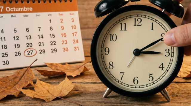 Primer plano de un reloj de manecillas clásicas marcando las tres de la madrugada junto a un calendario de otoño con hojas secas decorativas sobre una mesa de madera