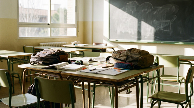 Material escolar, libros de texto y mochilas sobre un pupitre de madera en un aula iluminada con motivo de la vuelta al cole