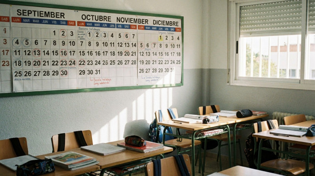Aula escolar con libros de texto y un calendario escolar de pared abierto en los meses del primer trimestre con fechas marcadas