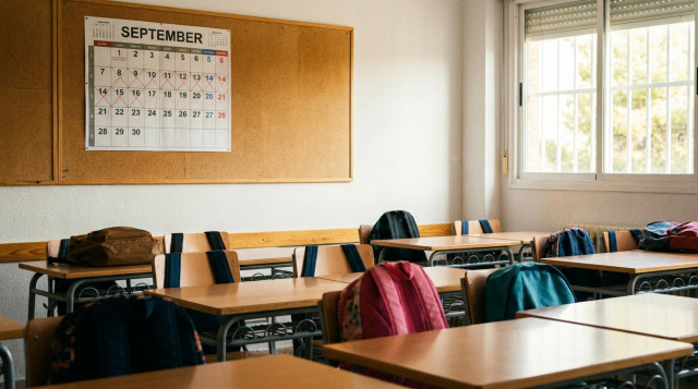 Aulas escolares preparadas con pupitres y mochilas con el calendario escolar de septiembre en un panel informativo
