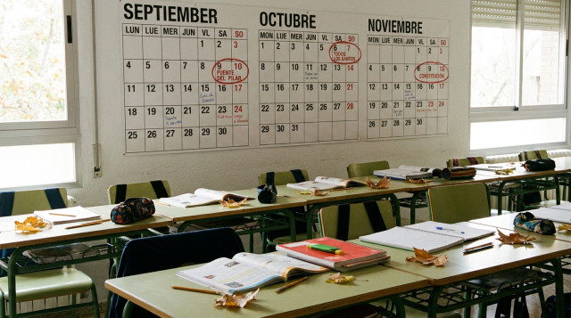 Aula escolar vacía con un calendario de pared de fondo señalando los meses de otoño y materiales educativos sobre las mesas