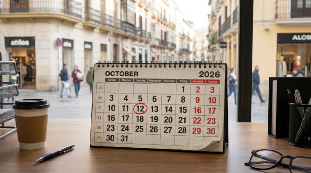 Calendario laboral de octubre sobre una mesa de trabajo con el día 12 marcado y calles comerciales de fondo