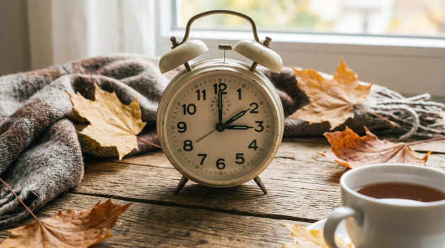 reloj despertador de pared sobre una mesa de madera con las manecillas marcando el cambio de hora de otoño en horario de invierno