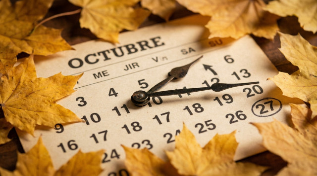 Manecillas de reloj vintage retrasándose una hora sobre fondo de calendario otoñal con hojas doradas