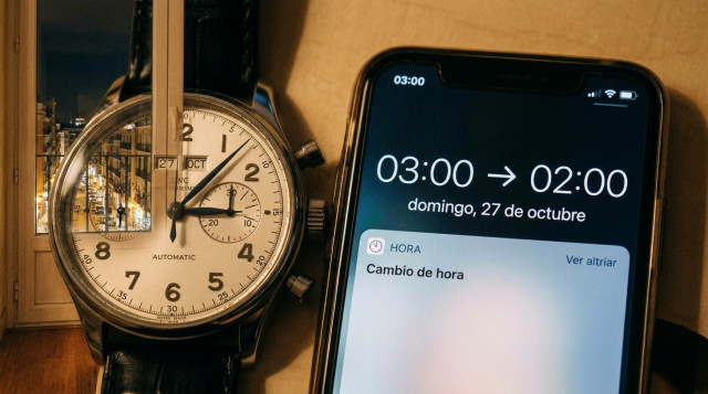 Primer plano de un reloj de pulsera mecánico y un smartphone sincronizando automáticamente la medianoche con el cambio de hora en octubre en España