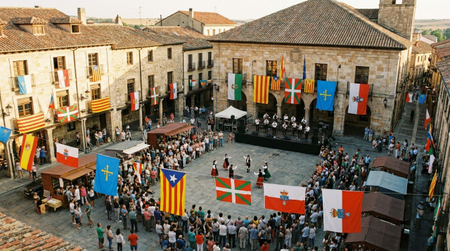 Vista aérea de una plaza histórica española decorada durante una festividad regional de septiembre con ambiente festivo y banderas autonómicas