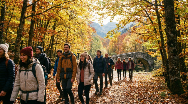 viajeros caminando por un sendero otoñal de bosque caducifolio con hojas doradas durante el puente de octubre