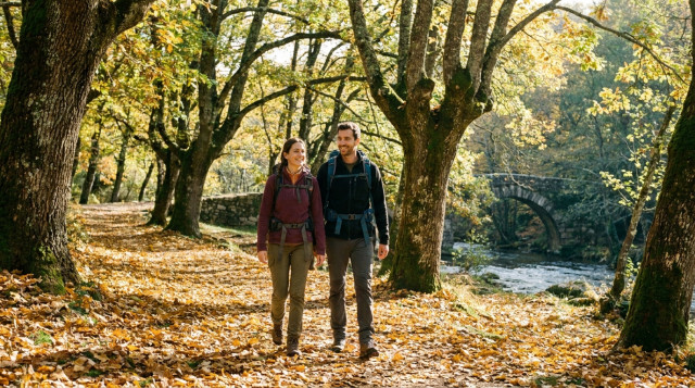pareja de senderistas caminando por un sendero cubierto de hojas doradas en un bosque de otoño durante el puente de Todos los Santos