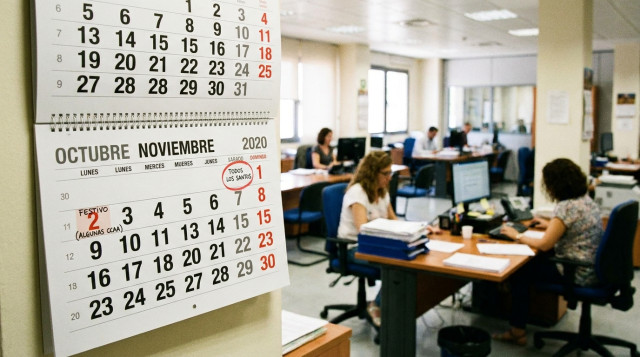Calendario de pared abierto en los meses de octubre y noviembre con el día 1 de noviembre marcado en domingo y oficinas administrativas de fondo